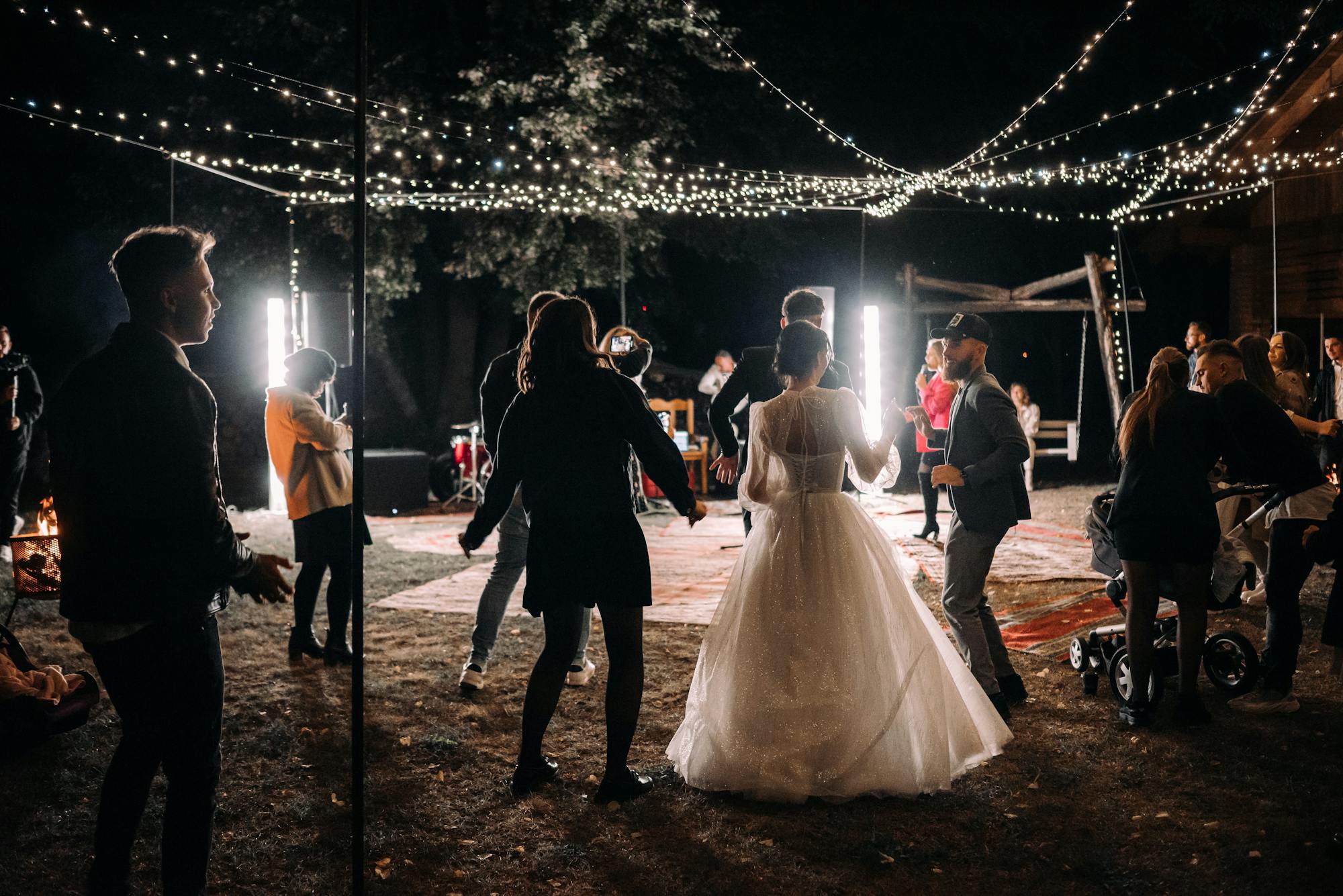 Bride and guests dancing under string lights at night