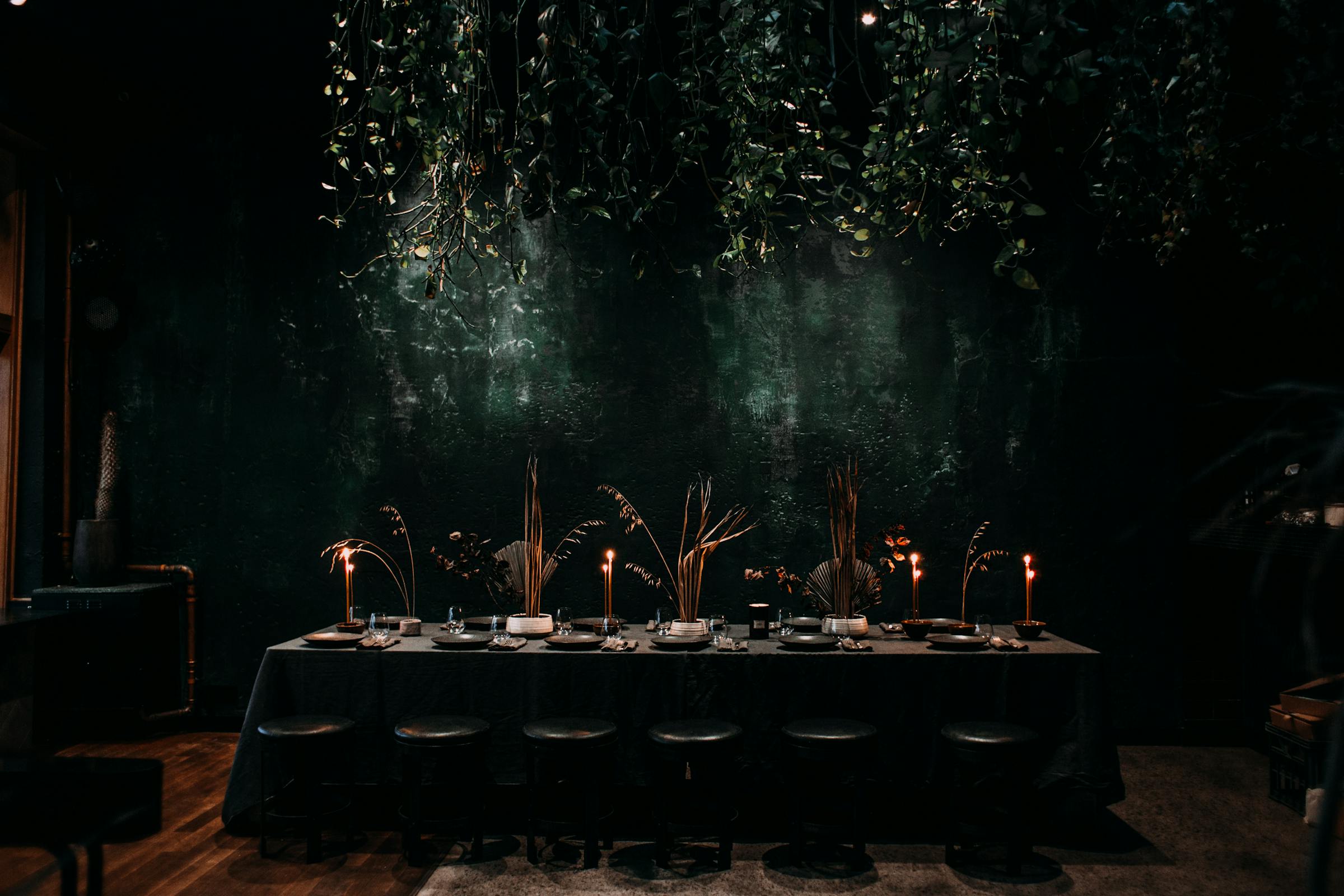 Moody event space with long dressed table, taper candles and hanging greenery overhead