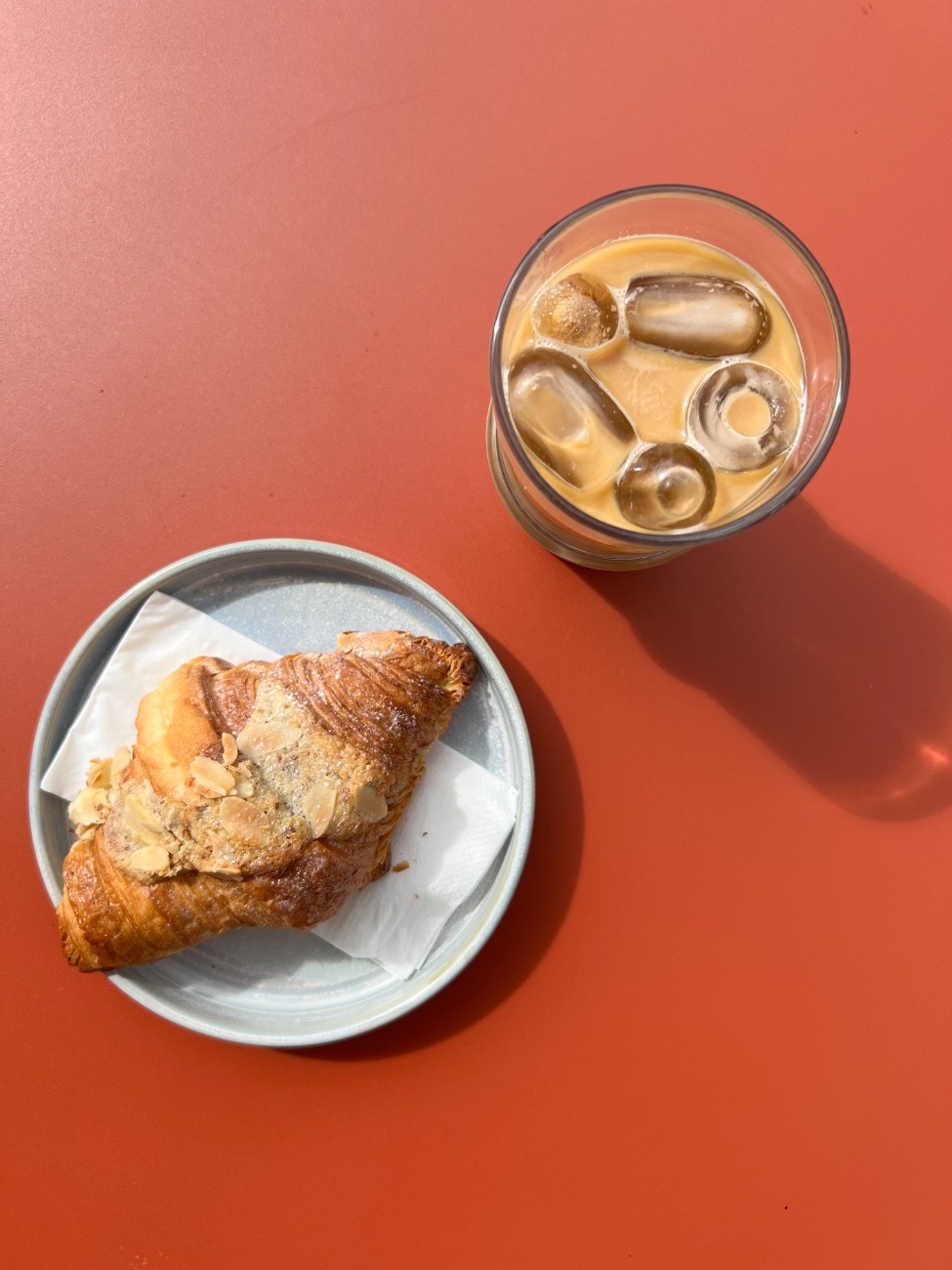 Iced coffee and an almond croissant on a terracotta table
